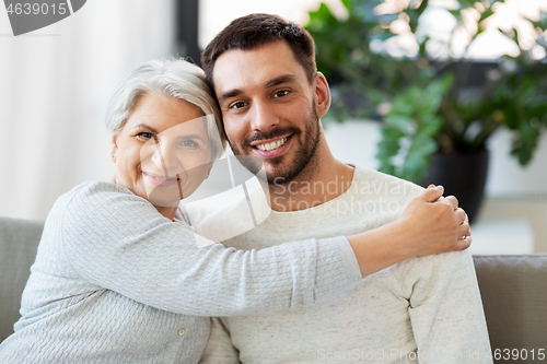 Image of senior mother with adult son hugging at home