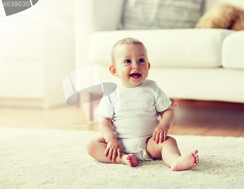 Image of happy baby boy or girl sitting on floor at home