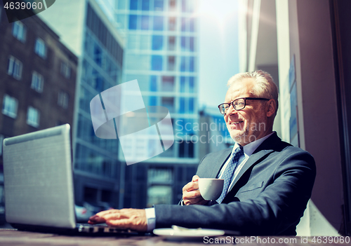 Image of senior businessman with laptop drinking coffee