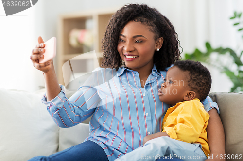 Image of african mother with baby son taking selfie at home