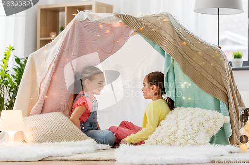 Image of happy girls lying in kids tent and talking at home