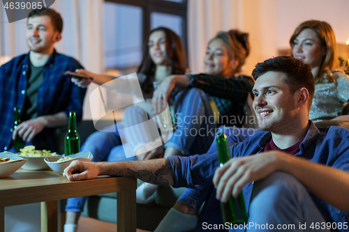 Image of happy friends with drinks watching tv at home