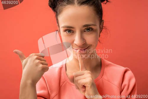 Image of The young woman whispering a secret behind her hand over coral background