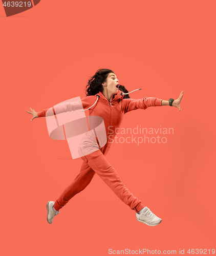 Image of Freedom in moving. Pretty young woman jumping against coral background