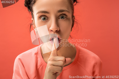 Image of The young woman whispering a secret behind her hand over coral background
