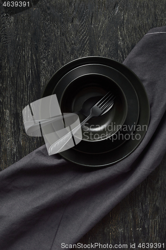 Image of Kitchen table served with black utensils ceramic plates, spoon, fork and textile napkin.