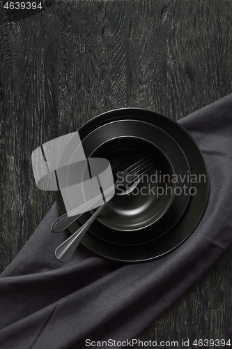 Image of Served kitchen table with black cookware ceramic plates, fork, spoon and textile napkin.