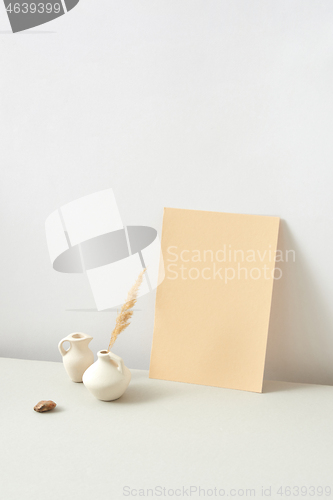 Image of Ceramic vases with dry natural twig and vertical paper sheet on a light grey background.