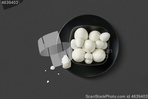 Image of Fresh farm chicken and quail eggs boiled on a black plate on a dark background.