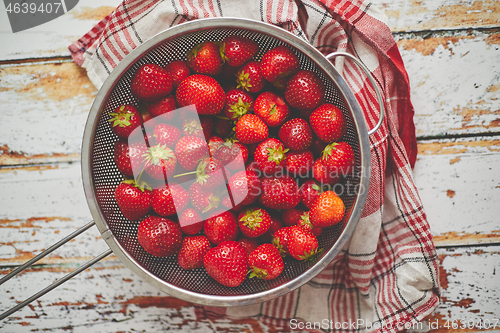 Image of Freshly harvested strawberries. Metal colander filled with juicy fresh ripe strawberries on an table