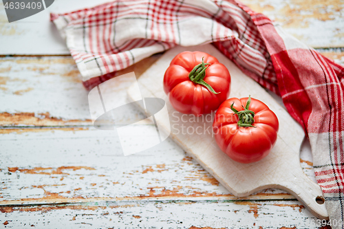 Image of Top view of a white cutting board with a fresh juicy tomatoes on a wooden table