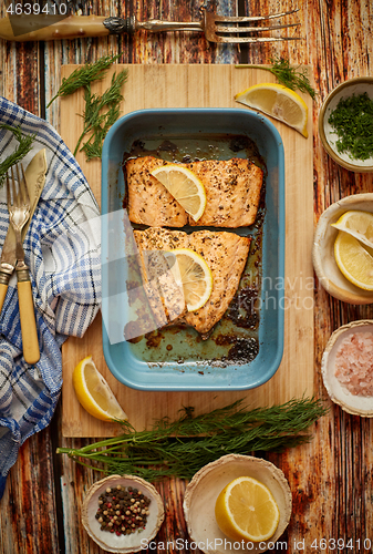 Image of Roasted salmon in heat proof dish. With aromatic dill, lemon, salt and pepper on sides.