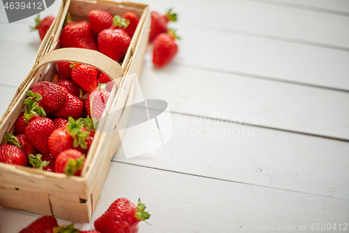 Image of Wooden container with fresh red strawberries. Placed on white table.