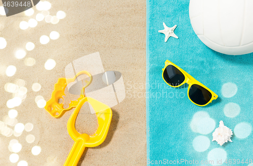 Image of sunglasses, sand toys and ball on beach towel