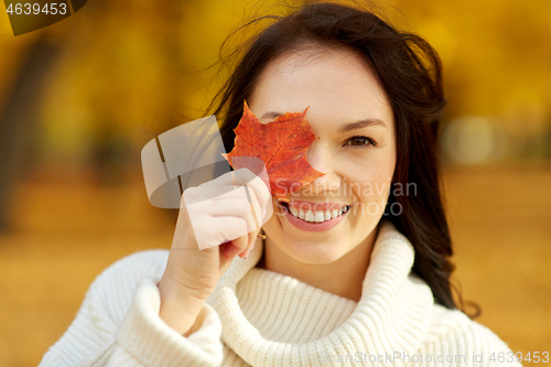 Image of happy young woman with maple leaf in autumn park