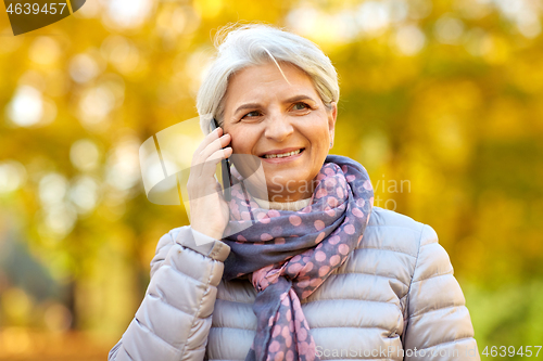 Image of senior woman calling on smartphone at autumn park