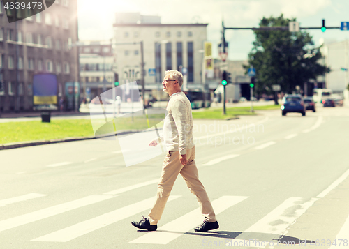 Image of senior man walking along city crosswalk