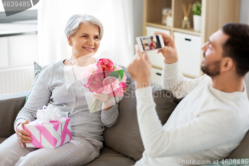 Image of adult son photographing senior mother at home