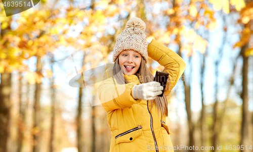 Image of girl taking selfie by smartphone at autumn park
