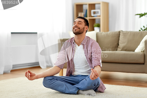 Image of man meditating in lotus pose at home