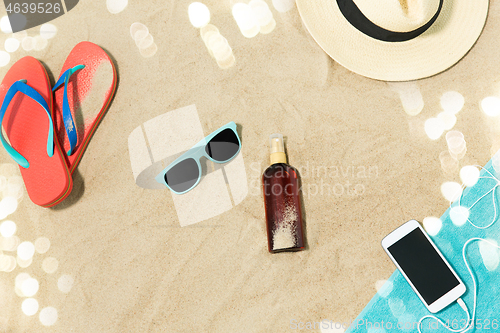 Image of smartphone, hat, flip flops and shades on beach