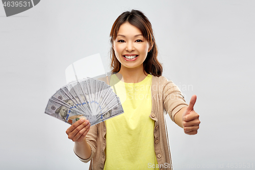 Image of asian woman with dollar money showing thumbs