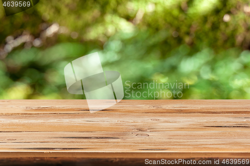 Image of Aged wooden table for montage or display products on a green leaves blurred background.