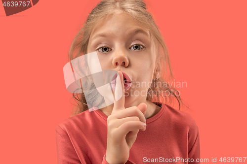 Image of Young girl with her finger on her mouth on coral background