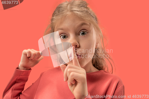 Image of Young girl with her finger on her mouth on coral background