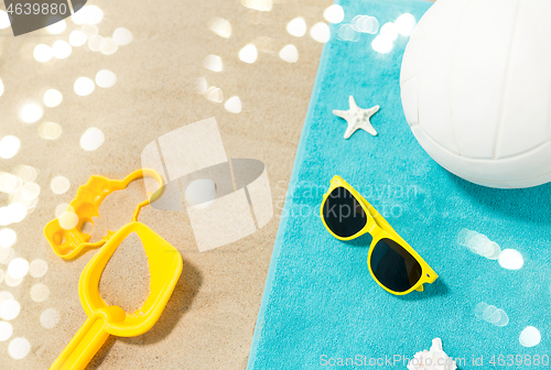 Image of sunglasses, sand toys and ball on beach towel