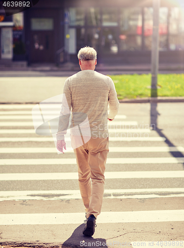 Image of senior man walking along city crosswalk