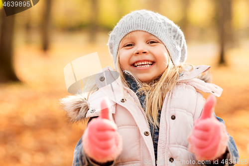 Image of happy little girl at autumn park showing thumbs up