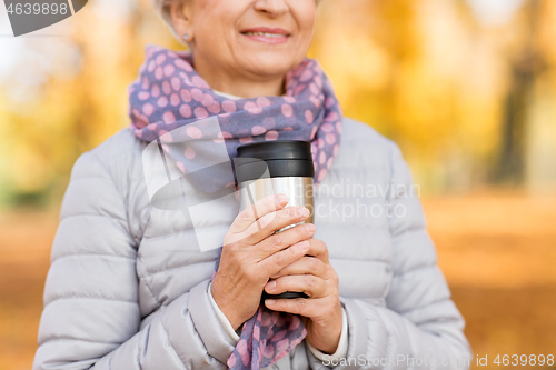 Image of old woman with hot drink in tumbler at autumn park