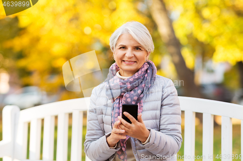 Image of happy senior woman with smartphone at autumn park
