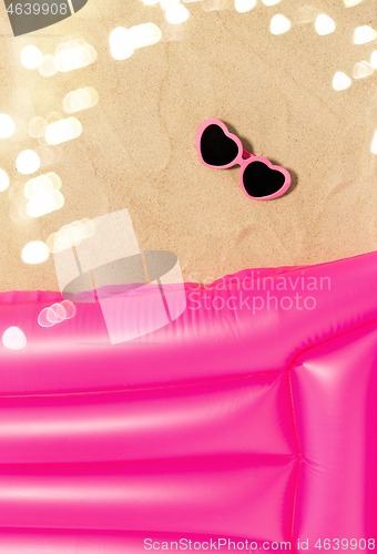 Image of sunglasses and pink swimming mattress on beach