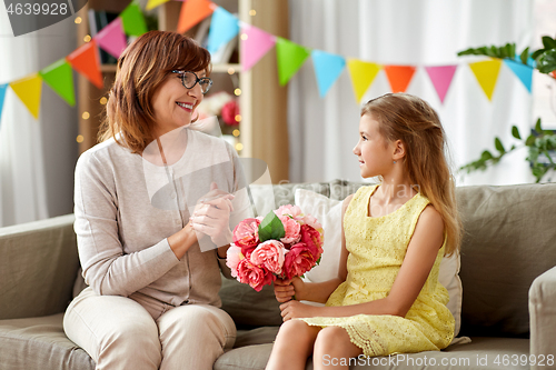 Image of granddaughter giving grandmother flowers at home