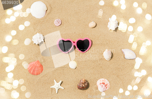 Image of heart-shaped sunglasses and shells on beach sand