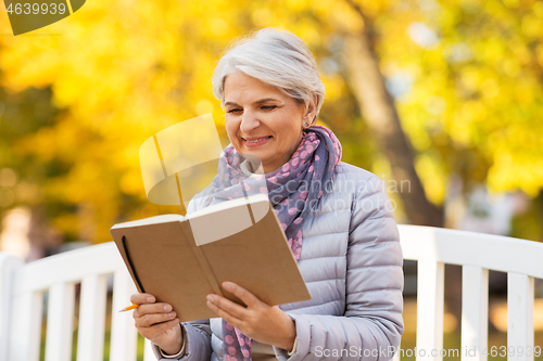 Image of happy senior woman reading diary at autumn park