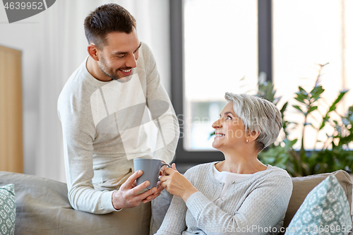 Image of adult son bringing coffee to senior mother at home