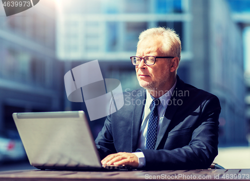 Image of senior businessman with laptop at city street cafe