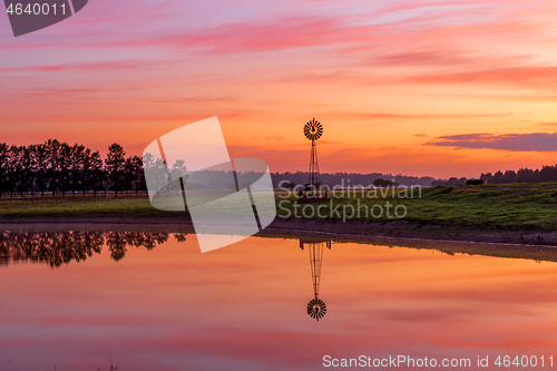 Image of Windmill sits on farm land with beautiful sunrise sky