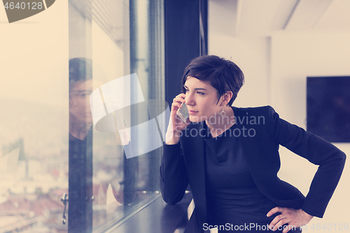 Image of Elegant Woman Using Mobile Phone by window in office building