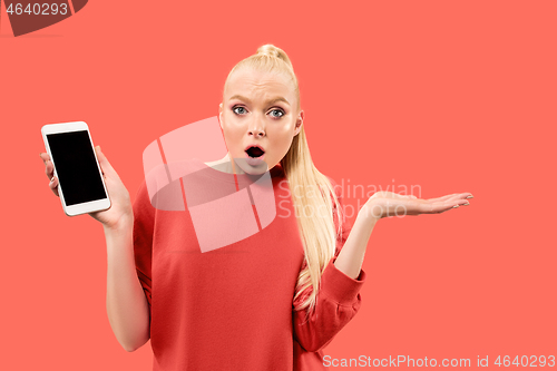 Image of Portrait of a confident casual girl showing blank screen mobile phone isolated over coral background