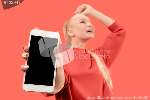 Image of Portrait of a confident casual girl showing blank screen mobile phone isolated over coral background