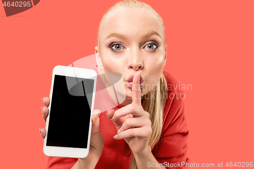 Image of Portrait of a confident casual girl showing blank screen mobile phone isolated over coral background