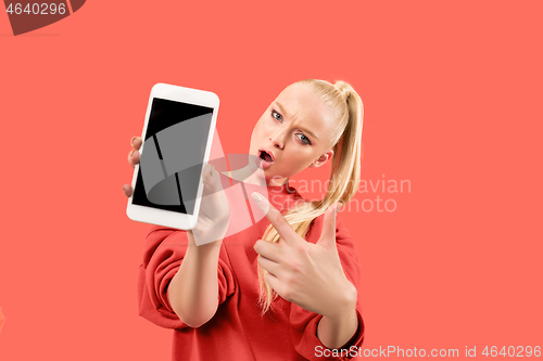 Image of Portrait of a confident casual girl showing blank screen mobile phone isolated over coral background