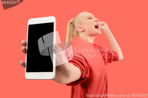 Image of Portrait of a confident casual girl showing blank screen mobile phone isolated over coral background