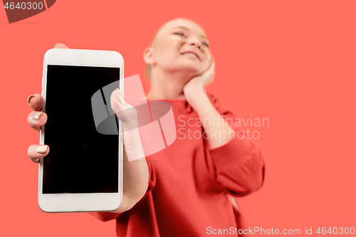 Image of Portrait of a confident casual girl showing blank screen mobile phone isolated over coral background