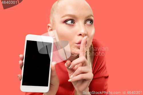 Image of Portrait of a confident casual girl showing blank screen mobile phone isolated over coral background