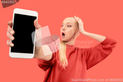 Image of Portrait of a confident casual girl showing blank screen mobile phone isolated over coral background